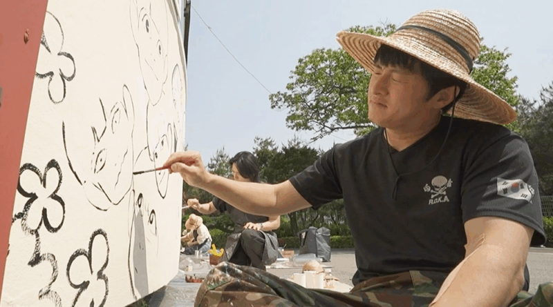 I Live Alone member paints mural with junior artists in a colorful volunteer event